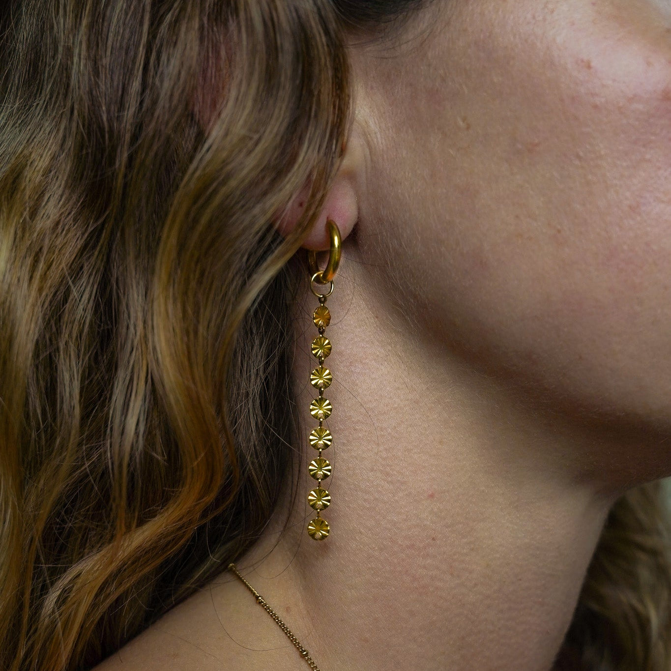 Close-up of a model wearing gold floral earrings, showcasing their elegant design.
