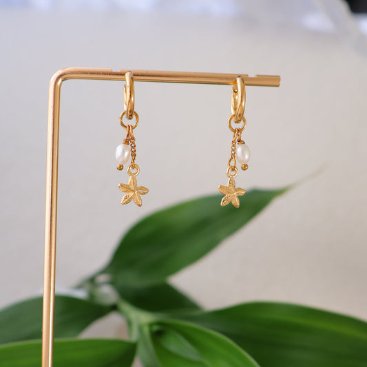 Gold earrings on a stand with green leaves in the background