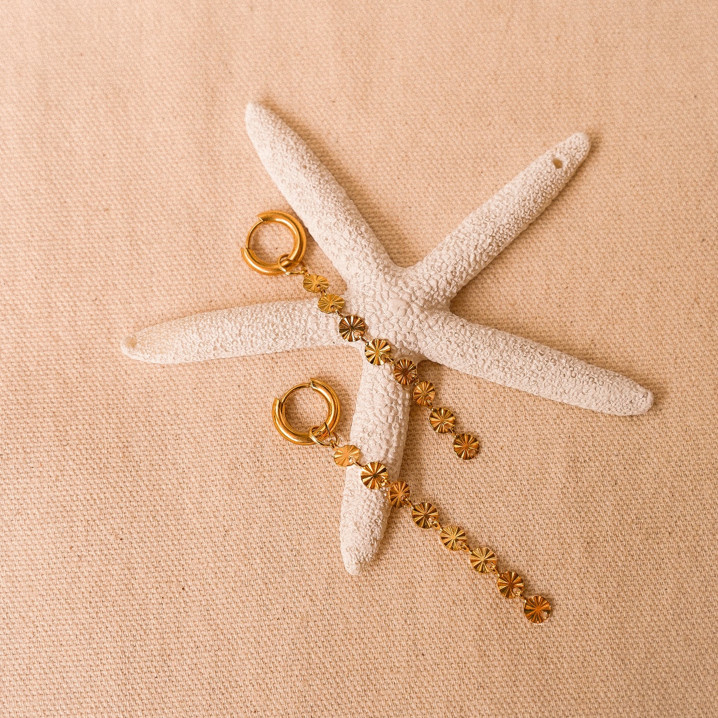 Solar inspired earrings featuring a removable sun charm on a starfish backdrop.