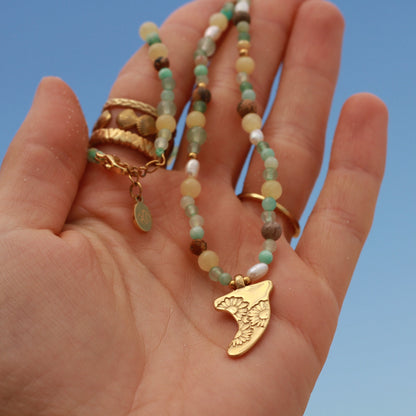 Hand holding a beaded necklace with a gold pendant against a clear blue sky