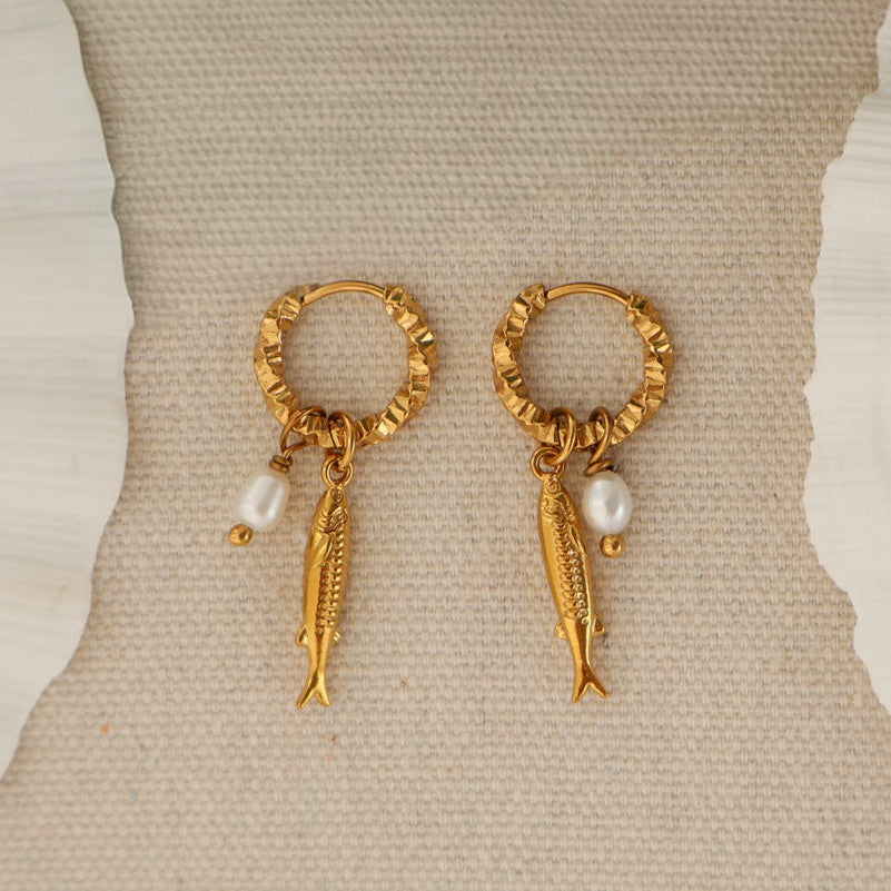 A pair of gold hoop earrings with dangling fish charms and small pearl beads