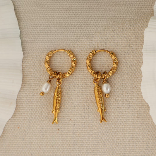 A pair of gold hoop earrings with dangling fish charms and small pearl beads