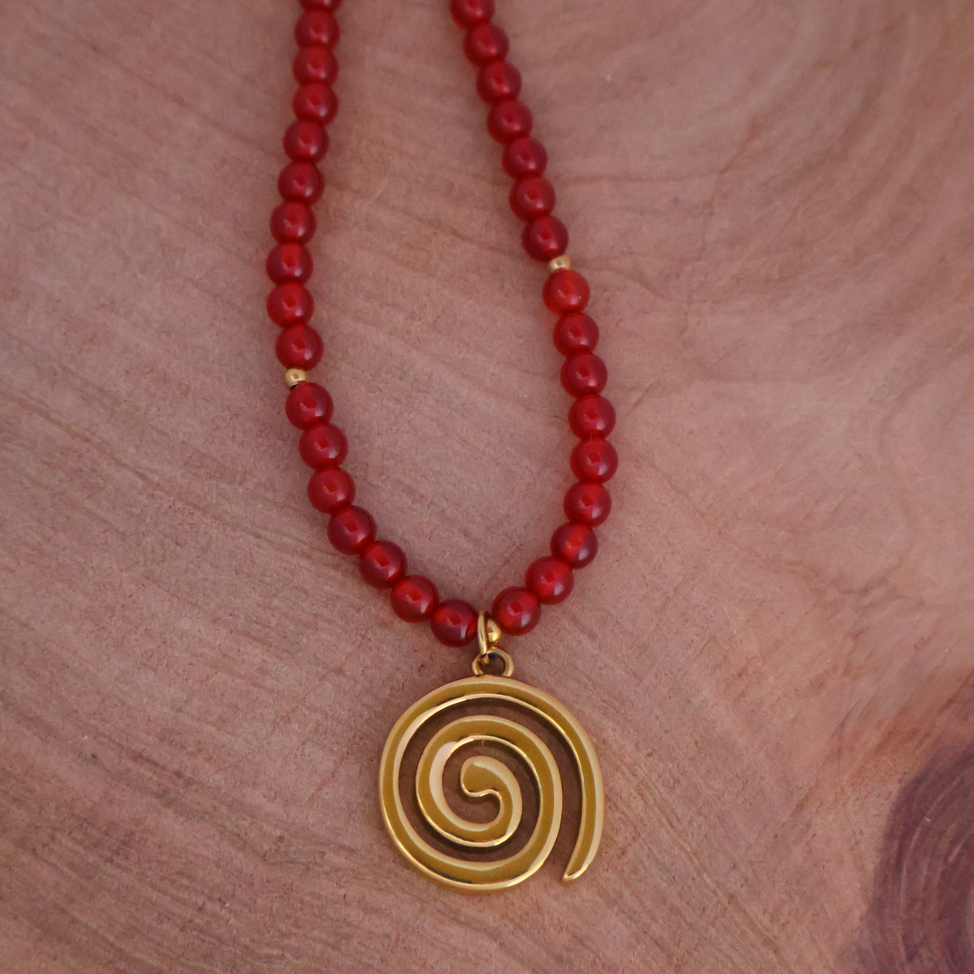 Swirl Necklace featuring red carnelian spiral necklace with gold pendant on red bead chain, symbolizing growth and transformation.