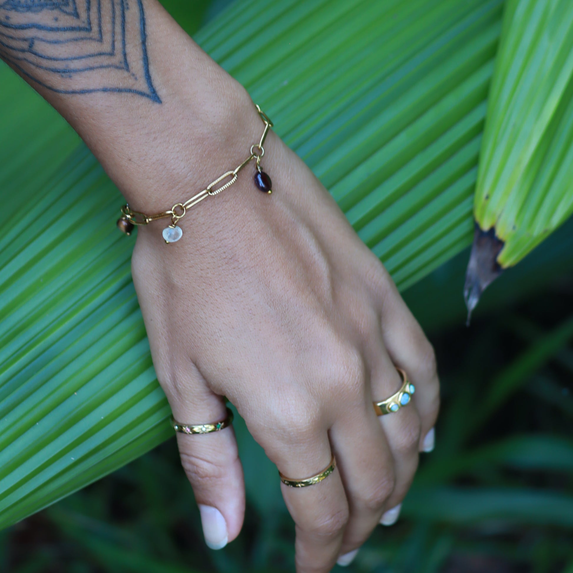 Hand with gold jewelry against a green leafy background
