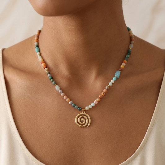 A close-up of a person wearing a beaded necklace with a gold spiral pendant. The necklace features small multicolored beads in pastel shades of orange, teal, light blue, and white.