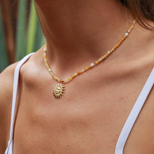 Necklace with a sun pendant worn by a person, with a blurred natural background
