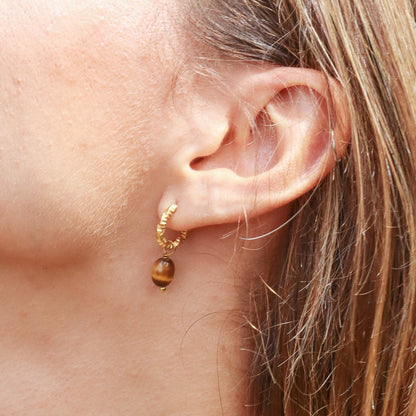 Close-up of a woman's ear with a gold earring against a green leafy background