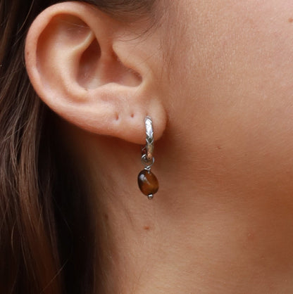 Close-up of an ear wearing a silver earring with a brown gemstone.