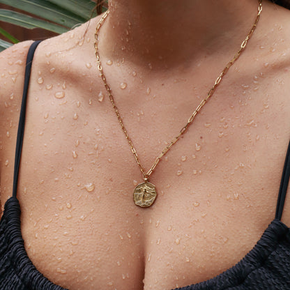 Gold necklace with a pendant on a person with water droplets on their skin.