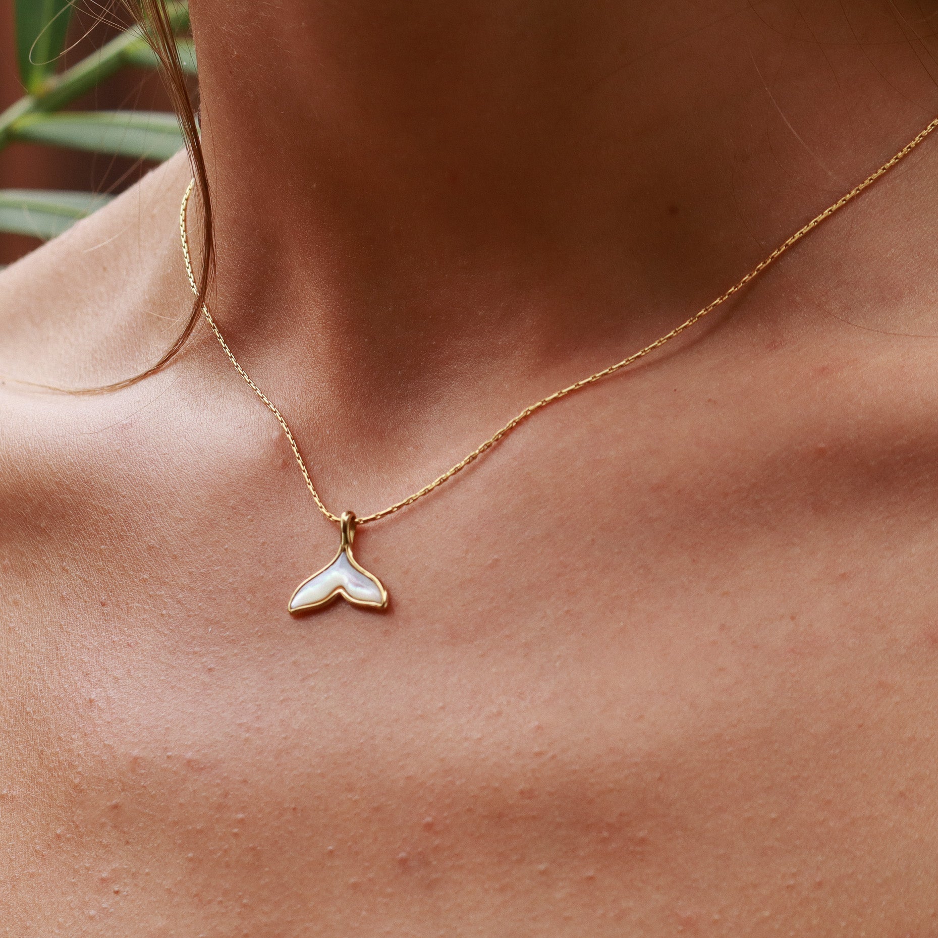 Gold necklace with a whale tail pendant on a person's neck