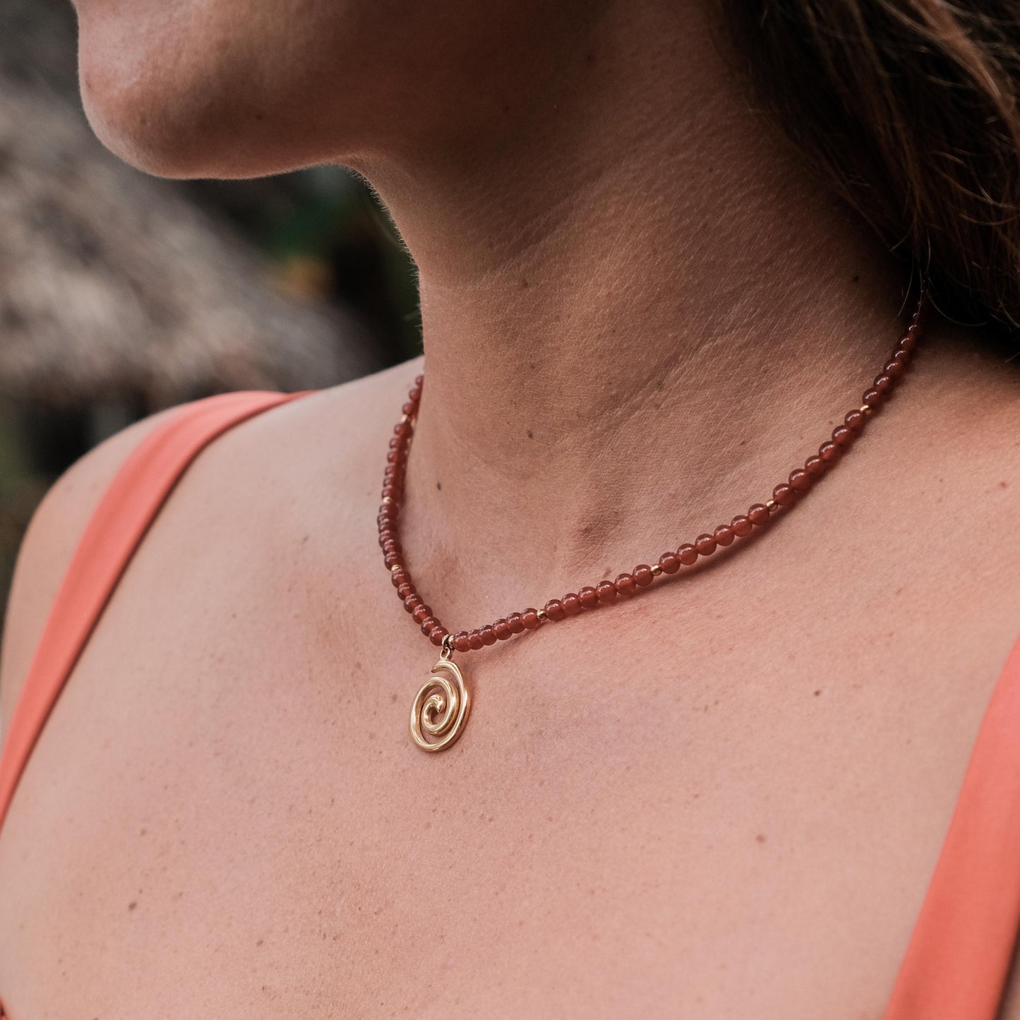 Person wearing a coral tank top and a necklace with a spiral pendant.