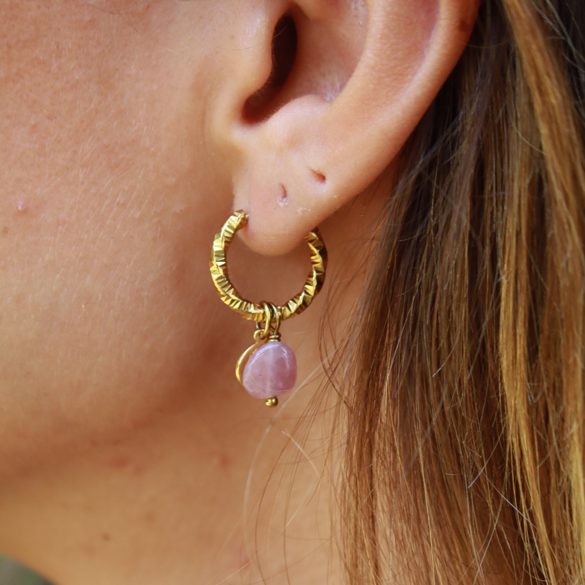 Close-up of an ear with a gold hoop earring featuring a pink gemstone.