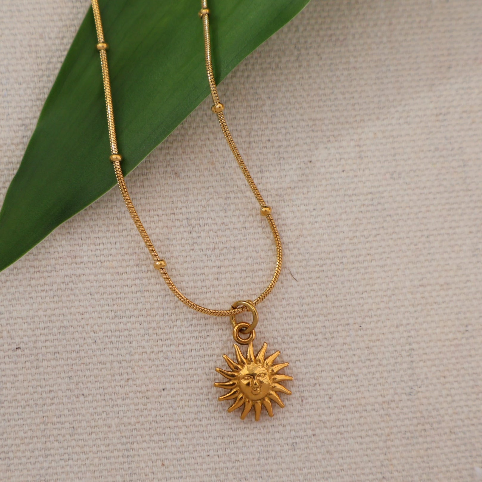 Gold necklace with a sunflower pendant on a textured beige background