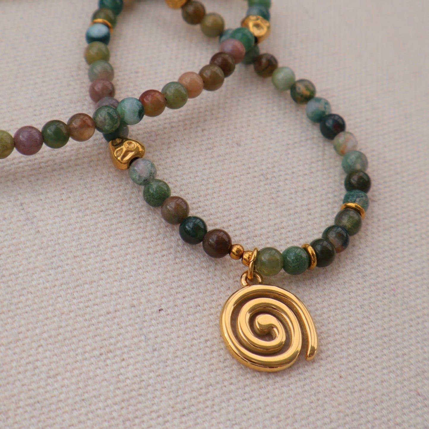 Beaded bracelets with gold spiral charm on a neutral background