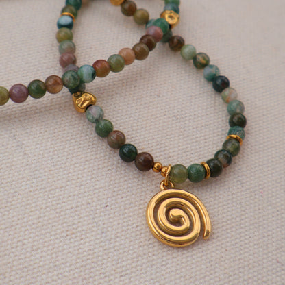 Beaded bracelets with gold spiral charm on a neutral background