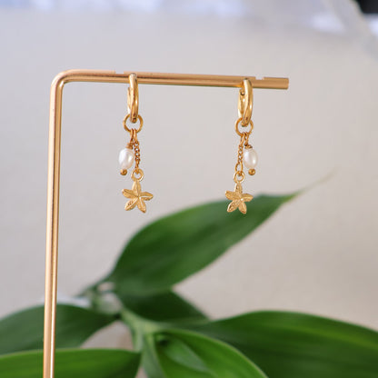 Gold earrings on a stand with green leaves in the background