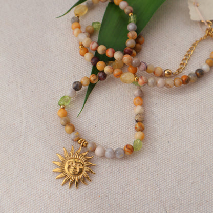 Beaded bracelet with sun charm on a textured surface with green leaves