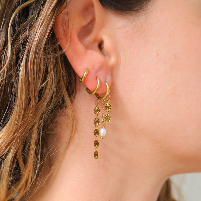 Close-up of an ear wearing gold hoop earrings with additional gold earrings featuring pearls.