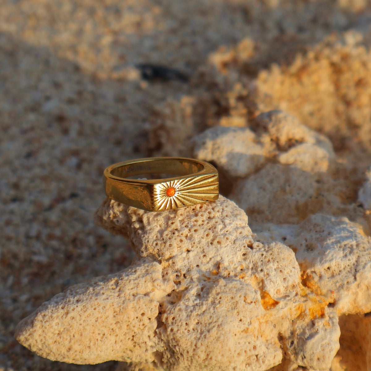 Gold ring with a sun design on a textured stone surface