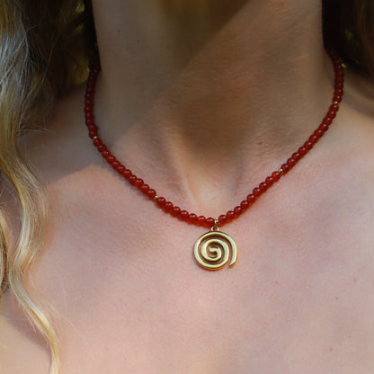 Red carnelian spiral necklace with gold spiral pendant, symbolizing growth and transformation, worn elegantly.