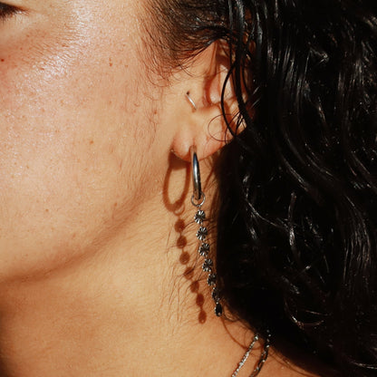 Close-up of a person wearing silver solar earrings featuring 10mm hoops and a removable dangly sun charm.
