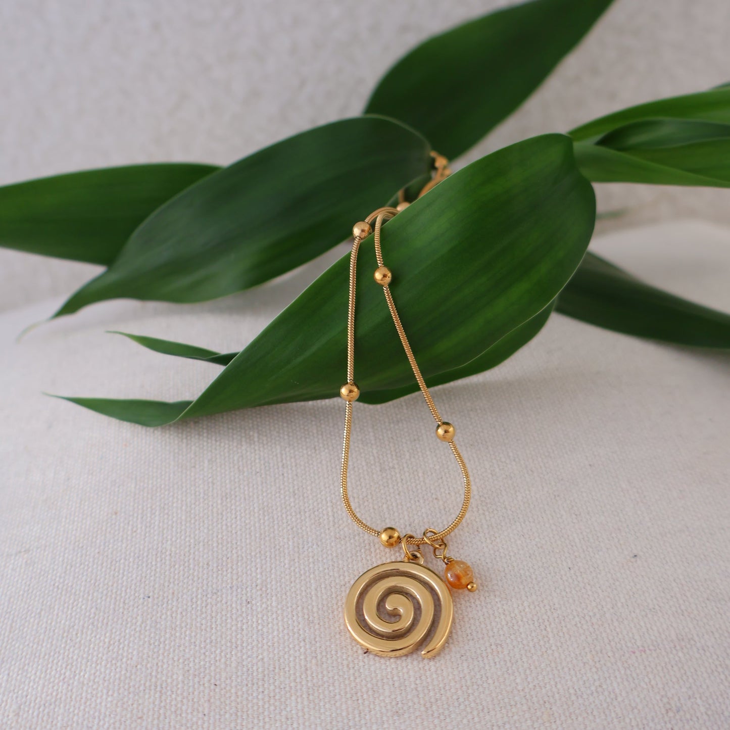 Gold spiral pendant on a green leaf against a light background